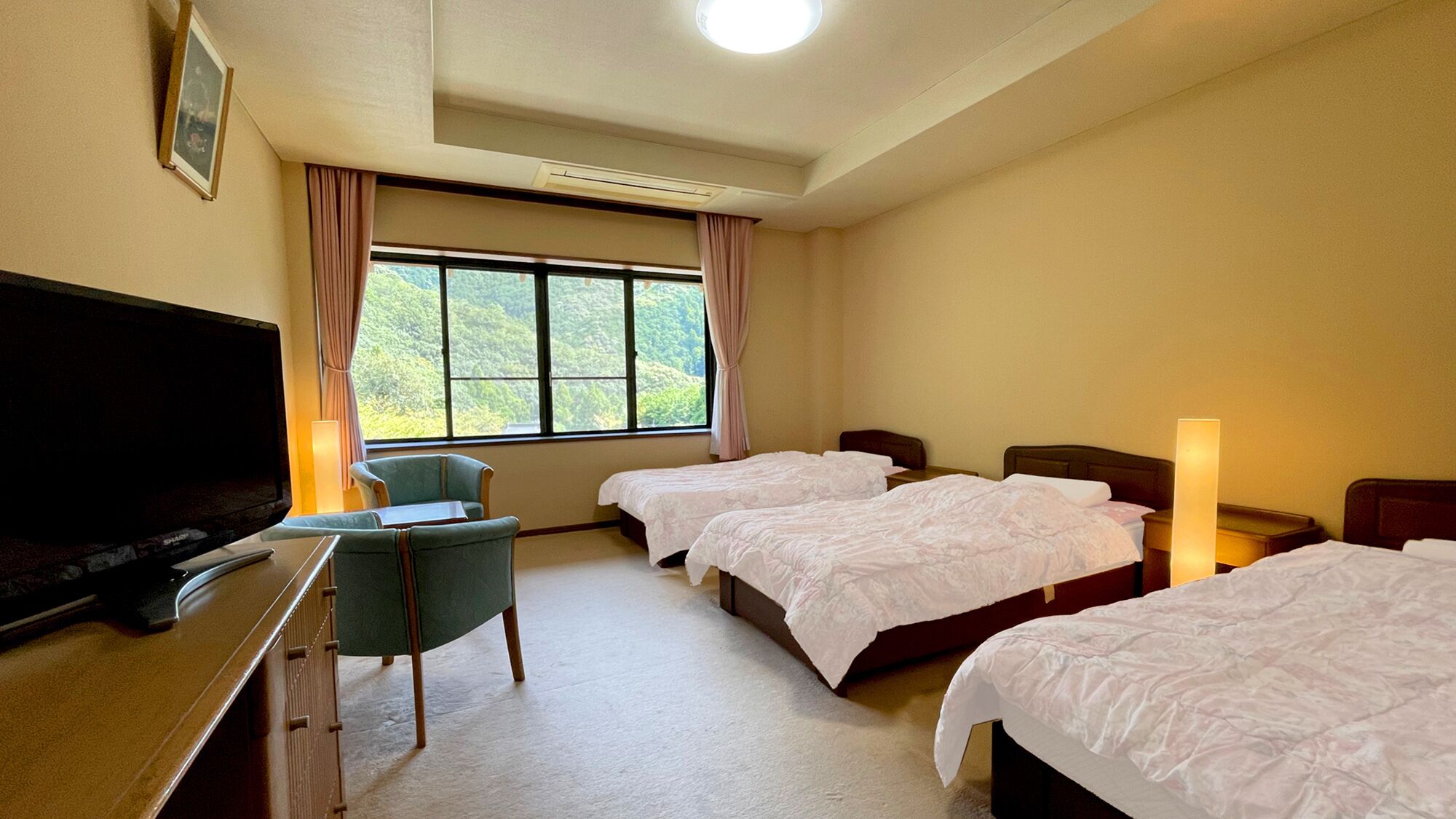 A hotel room with two beds, a desk with a television, a chair, and a window with curtains.