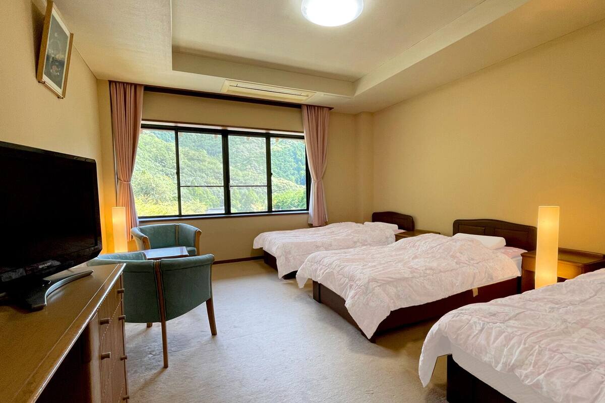 Une chambre d’hôtel avec deux lits, un bureau avec une télévision, une chaise et une fenêtre avec des rideaux.