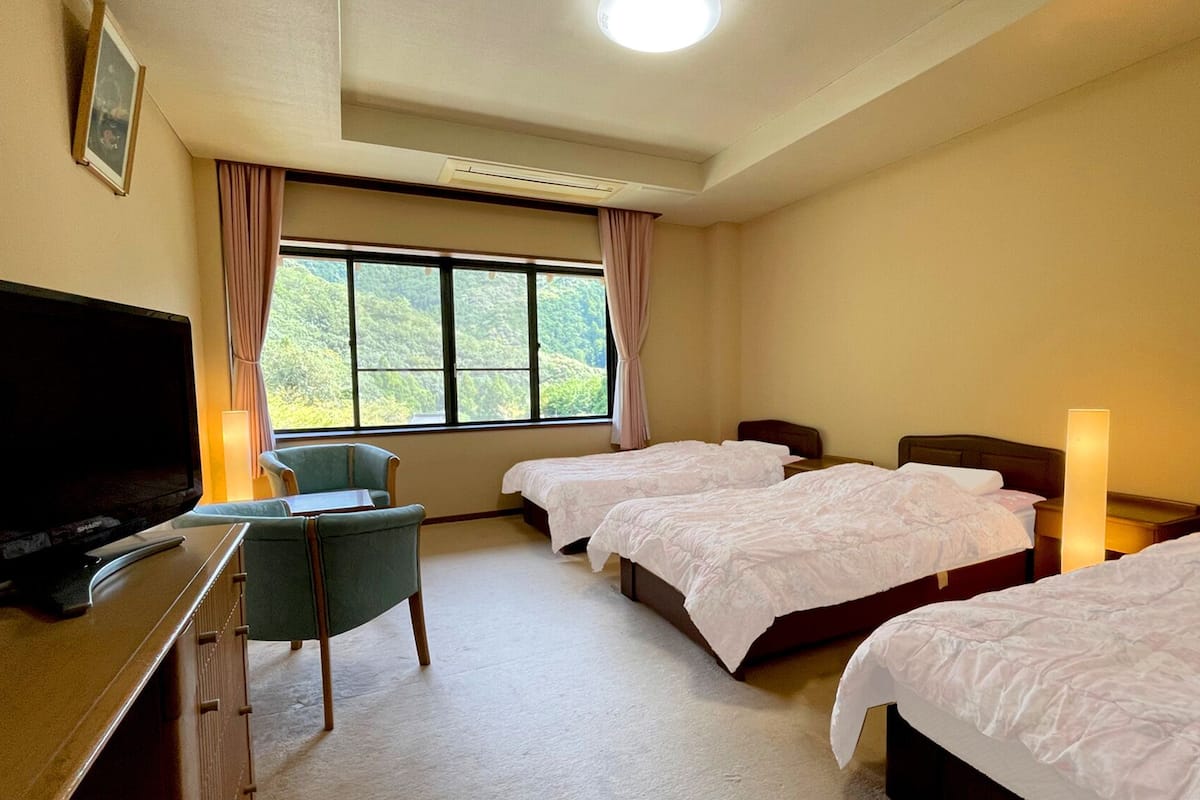 A hotel room with two beds, a desk with a television, a chair, and a window with curtains.