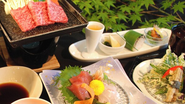 A variety of Japanese dishes including sashimi, a hot plate with meat, and a bowl of soup.