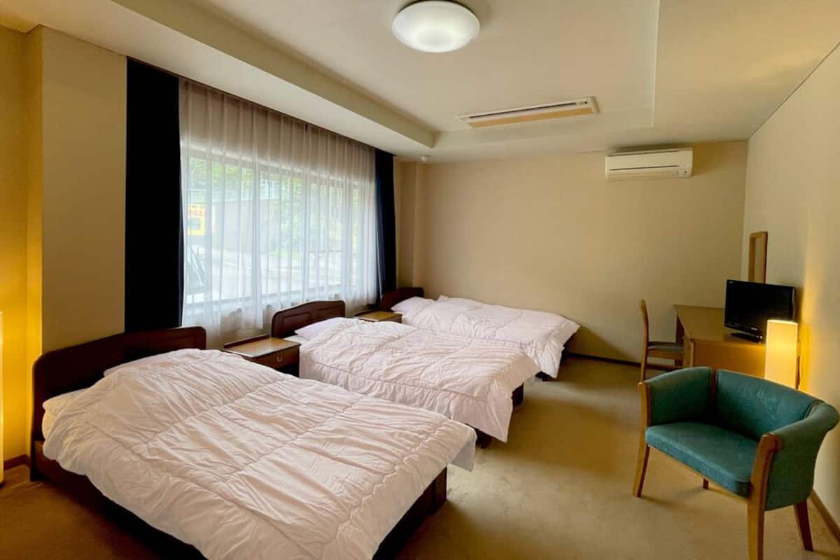 Une chambre d’hôtel avec deux lits, une télévision, une chaise et une fenêtre avec des rideaux.