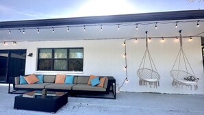 An outdoor seating area with a sofa and hanging chairs, string lights, and a window. - Vacation guest pool home (Naples)
