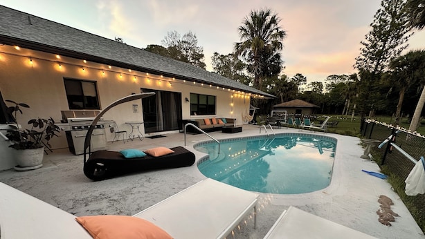 A backyard with a swimming pool, lounge chairs, and a barbecue grill. - Vacation guest pool home (Naples)