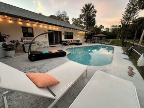 Un jardin avec une piscine, des chaises longues et un barbecue.