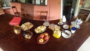 A breakfast setup with bread, apples, a glass of juice, and various breakfast items on a wooden table. - Pousada Cavalo de Pedra (Peruíbe)