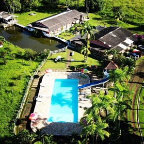 An aerial view of a resort with a swimming pool, a boat dock, and lush greenery. - Pousada Cavalo de Pedra (Peruíbe)