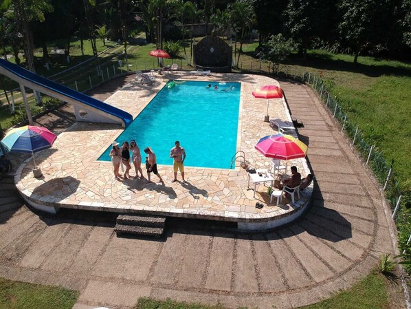 A swimming pool with a stone deck, surrounded by umbrellas and lounge chairs. - Pousada Cavalo de Pedra (Peruíbe)