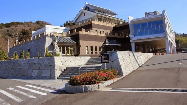 Un edificio de varios pisos con fachada de piedra, una escalera que lleva a la entrada y un cielo despejado.