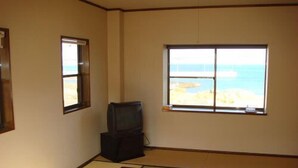 Una habitación con suelo de tatami, televisor y ventana con vista a la playa.
