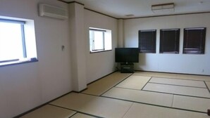 Una habitación con esteras de tatami, un televisor y tres ventanas.