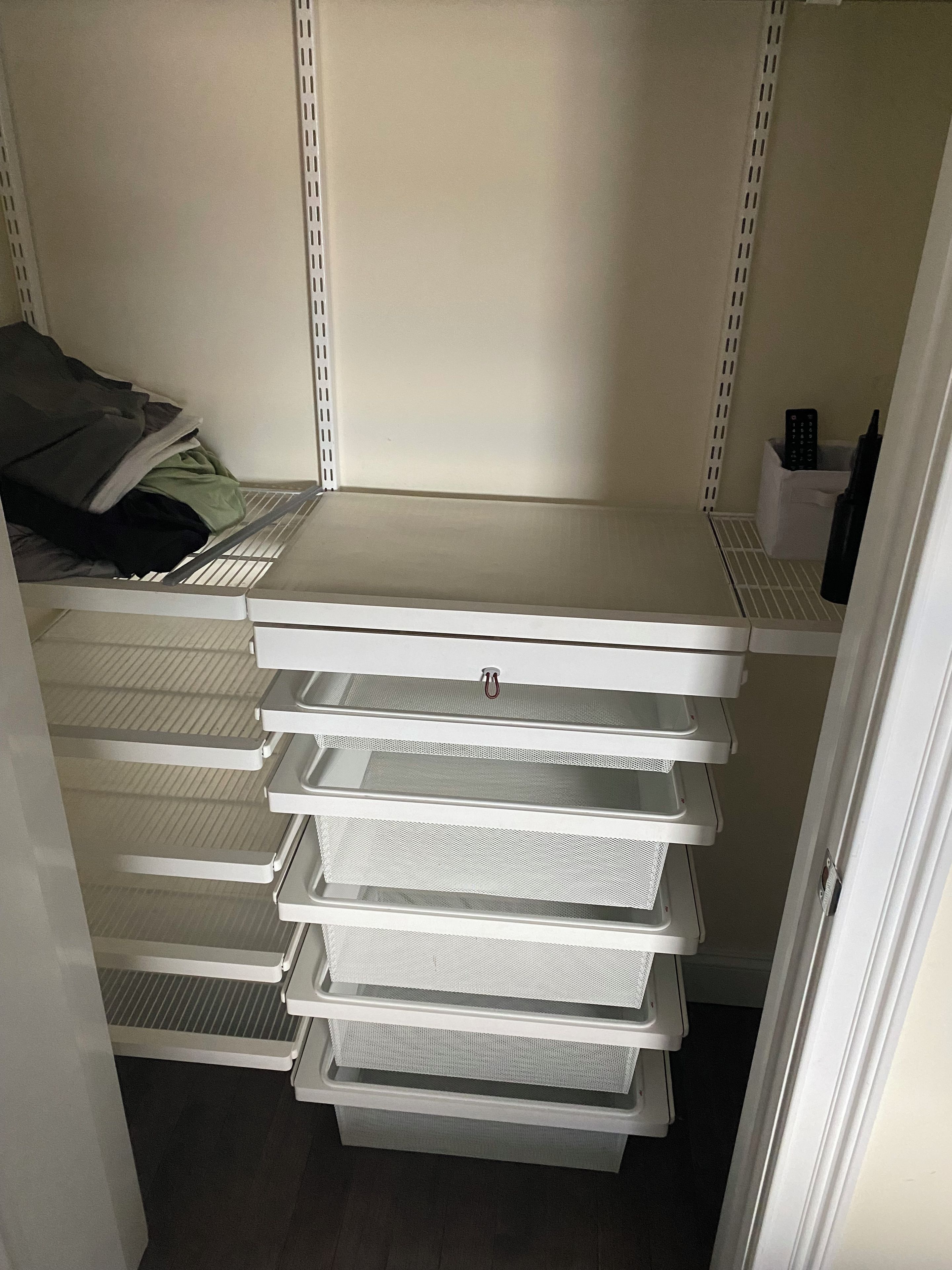 Un placard de rangement doté de plusieurs étagères et de tiroirs, dont certains contiennent des objets tels qu’une couverture et une télécommande.