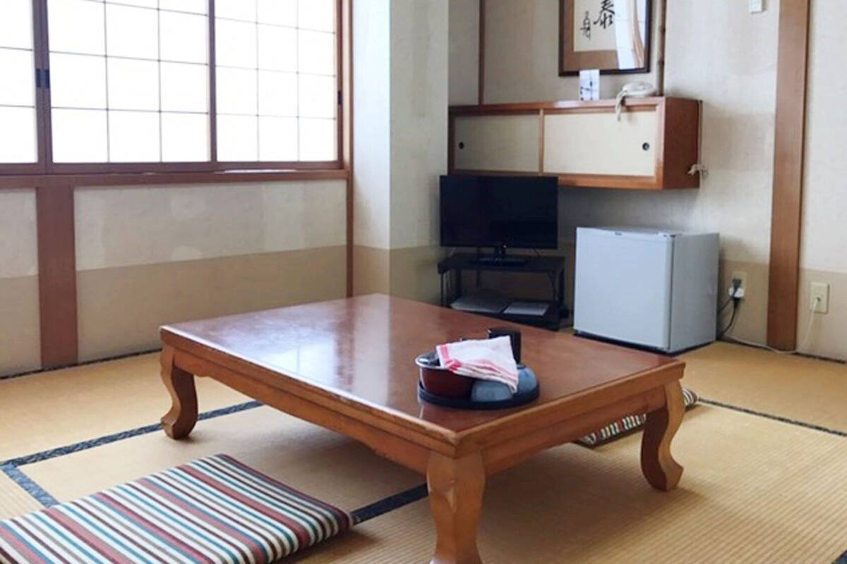 Una tradizionale stanza giapponese con pavimenti in tatami, un tavolo in legno, una televisione e un piccolo frigorifero.