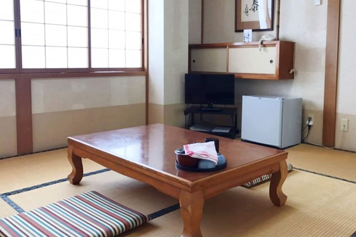 A traditional Japanese room with tatami flooring, a wooden table, a television, and a small refrigerator.