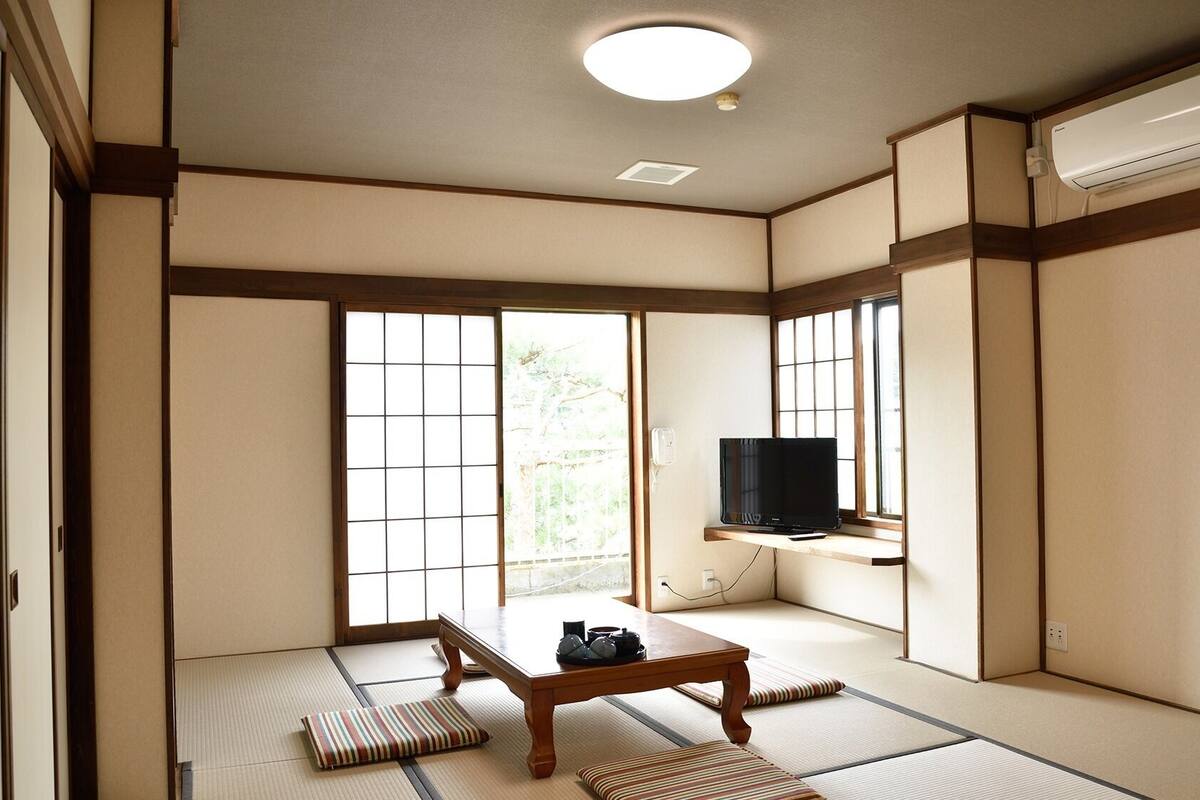 Una tradizionale stanza giapponese con pavimento in tatami, porte scorrevoli, un televisore su uno scaffale e un condizionatore d'aria.