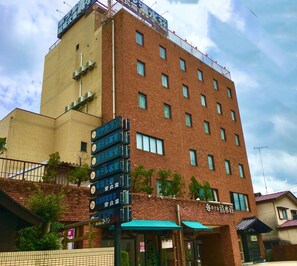 A multi-story hotel with a brick facade, multiple windows, and a sign indicating various hotel rooms and facilities. - Hotel Shimizuso (Sakura)