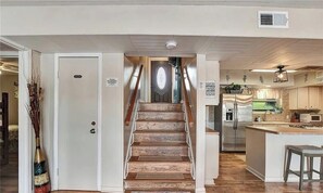 Eine Treppe führt zu einer Tür mit einem Schild, einer Küchenzeile inklusive Kühlschrank und einem Holzboden.