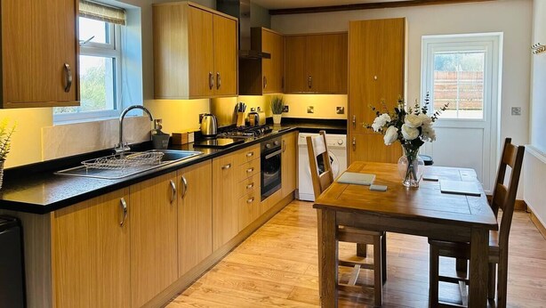 Une cuisine moderne avec des meubles en bois, un plan de travail noir et un coin repas comprenant une table et des chaises en bois.