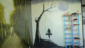 Una stanza con un murale raffigurante un sentiero boschivo e un'altalena, un mobiletto per scarpe blu e un letto con testiera bianca.