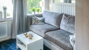 Ein gemütliches Zimmer mit einem grauen Sofa, einem weißen Nachttisch und einem Fenster mit Vorhängen.