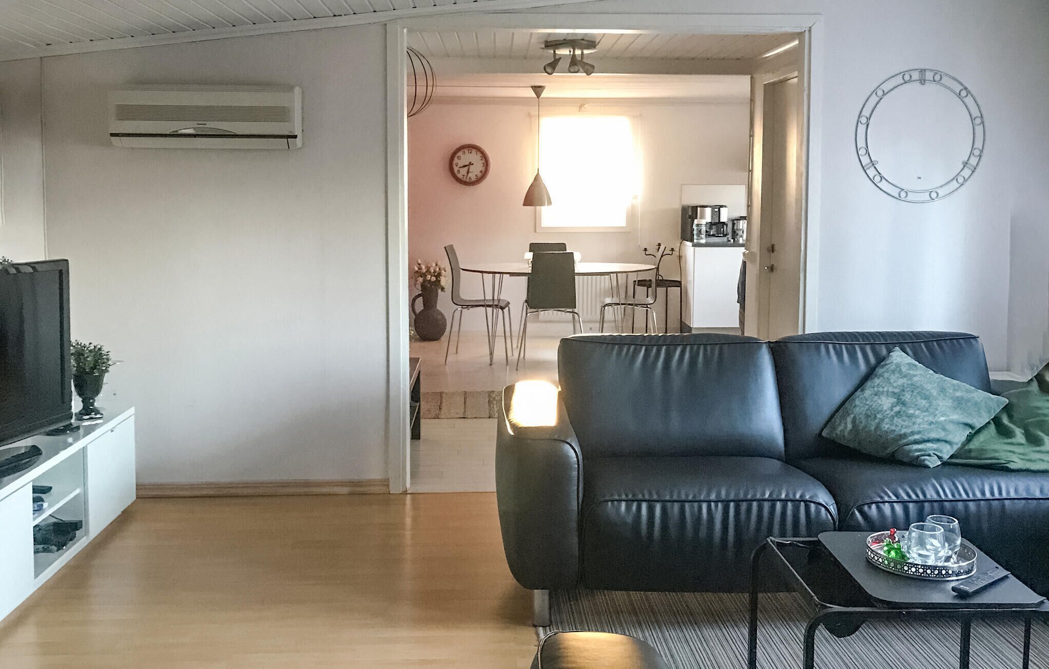 Un salon moderne avec un canapé en cuir noir, une table basse avec des verres et un plateau, et un téléviseur posé sur un meuble.