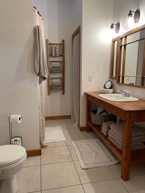 A bathroom with a toilet, sink, and mirror. There are towels and a basket on the counter.