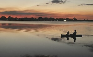 A calm lake at sunset with silhouettes of two people in a boat.
