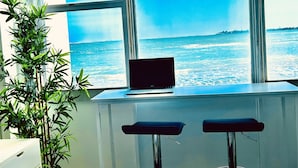Una computadora portátil sobre un escritorio con vista al océano a través de amplios ventanales.