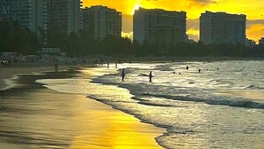 Una playa con edificios al fondo y gente caminando por la orilla.