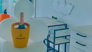 Una habitación moderna con una mesa blanca, una botella de champán amarillo en una copa y una decoración geométrica en la pared.