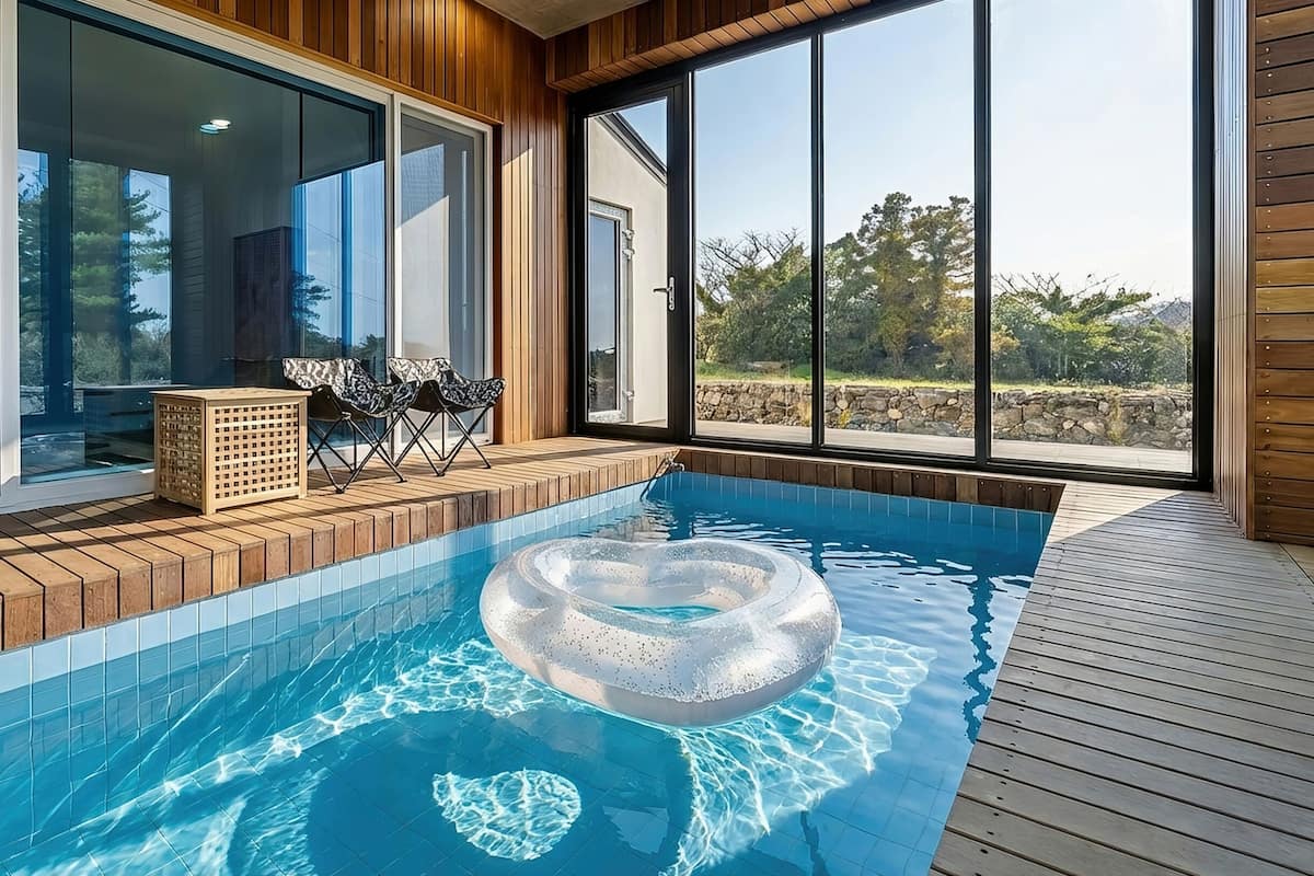 A modern indoor pool with a wooden deck, glass doors, and a view of the outdoors.