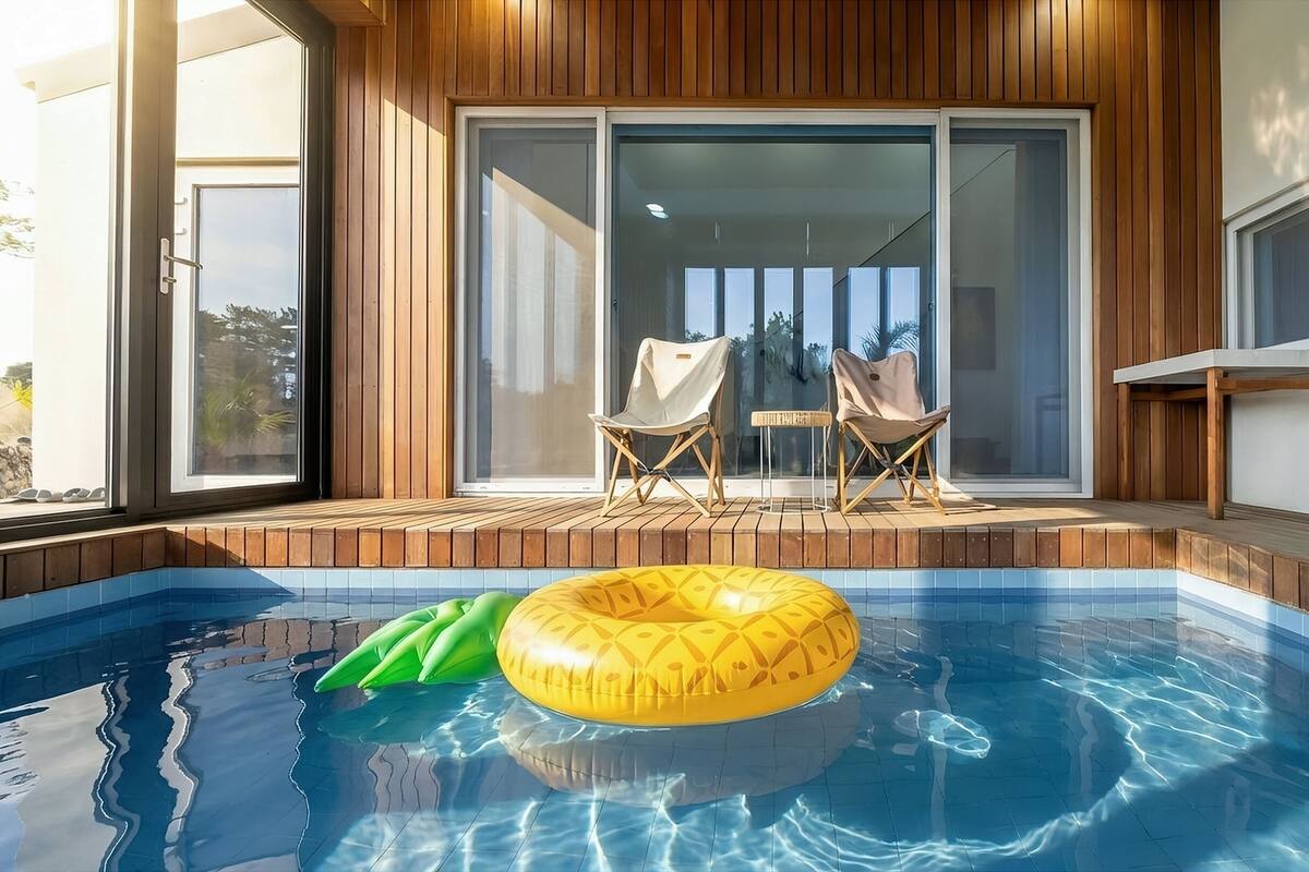 A modern outdoor pool area with a wooden deck, two lounge chairs, and a yellow inflatable ring.
