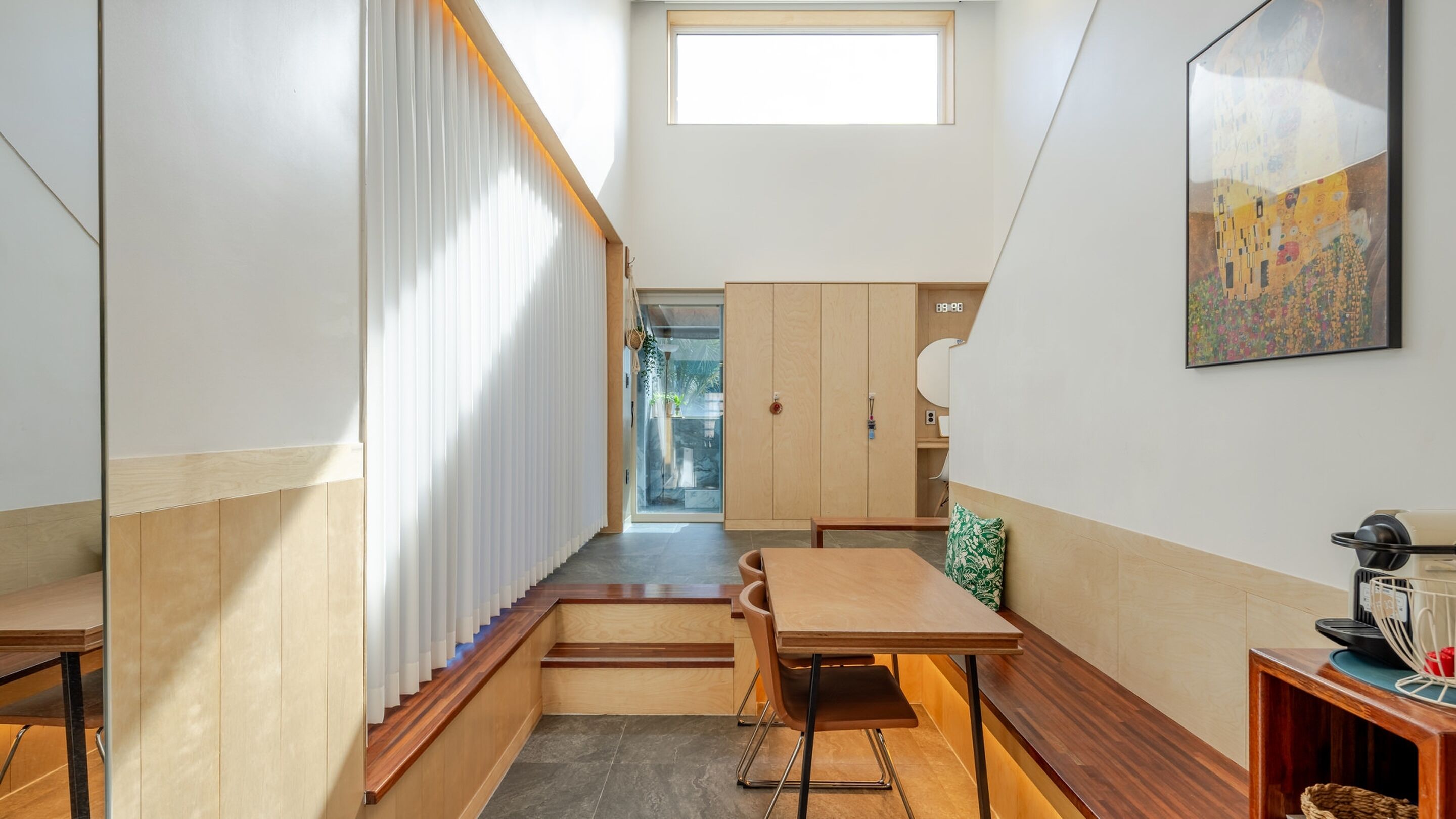 Un couloir étroit avec un plancher en bois, un escalier et un coin repas comprenant une table et des chaises.