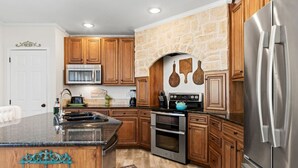 A modern kitchen with wooden cabinets, a stone wall, a stainless steel refrigerator, and a built-in oven.