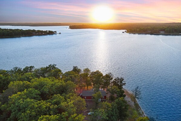 A lakeside property with a house surrounded by dense trees, offering a view of the lake and sunset.