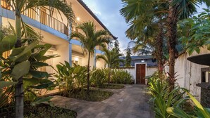 Une cour avec un chemin pavé, des palmiers et un bâtiment doté de balcons.