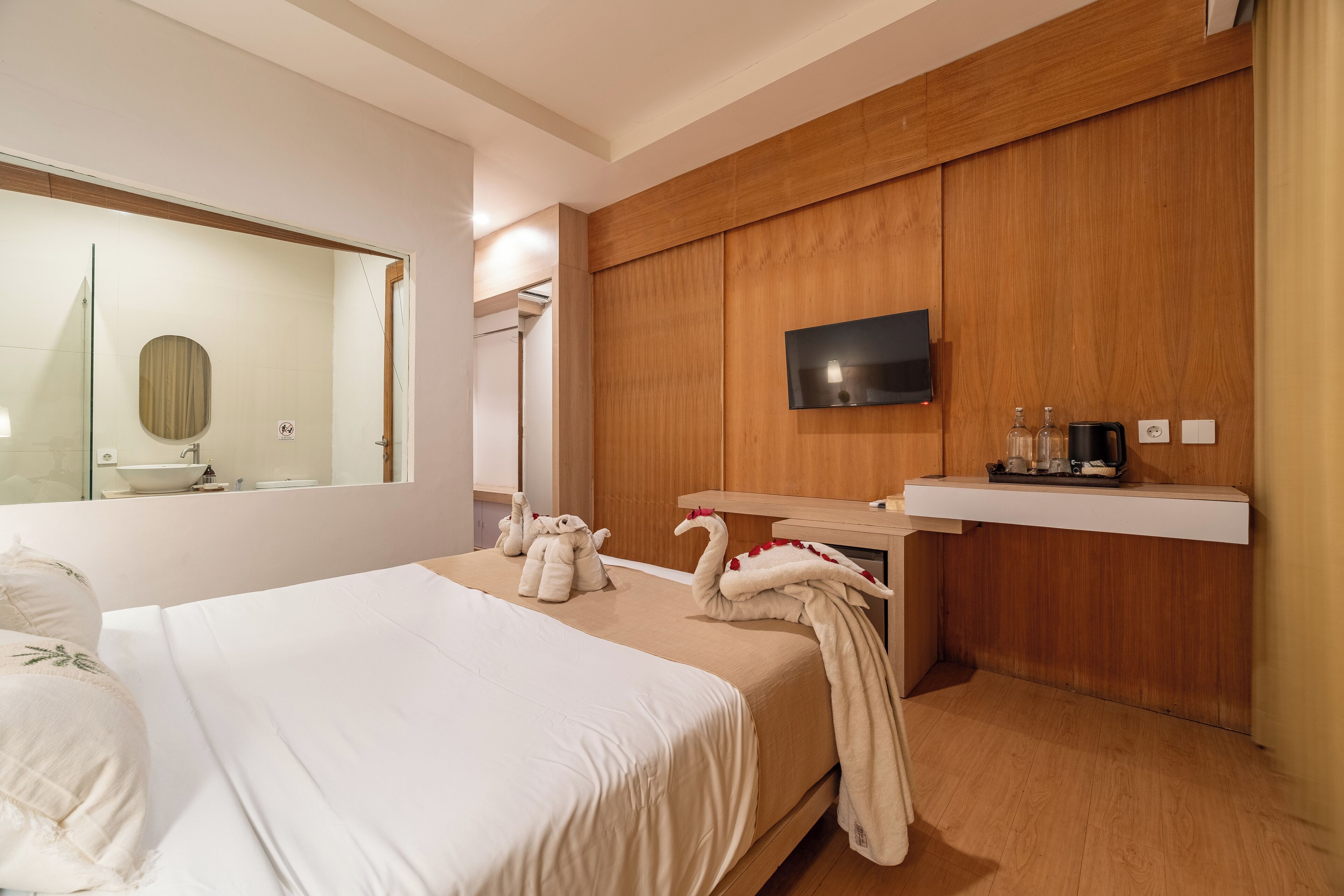 Een hotelkamer met een bed, een aan de muur bevestigde televisie, een houten paneelwand, een klein plankje met toiletartikelen en een spiegel.