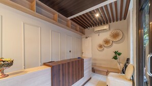 Un espace d’accueil doté d’un comptoir de réception en bois, de murs blancs et d’un plafond avec des poutres apparentes.