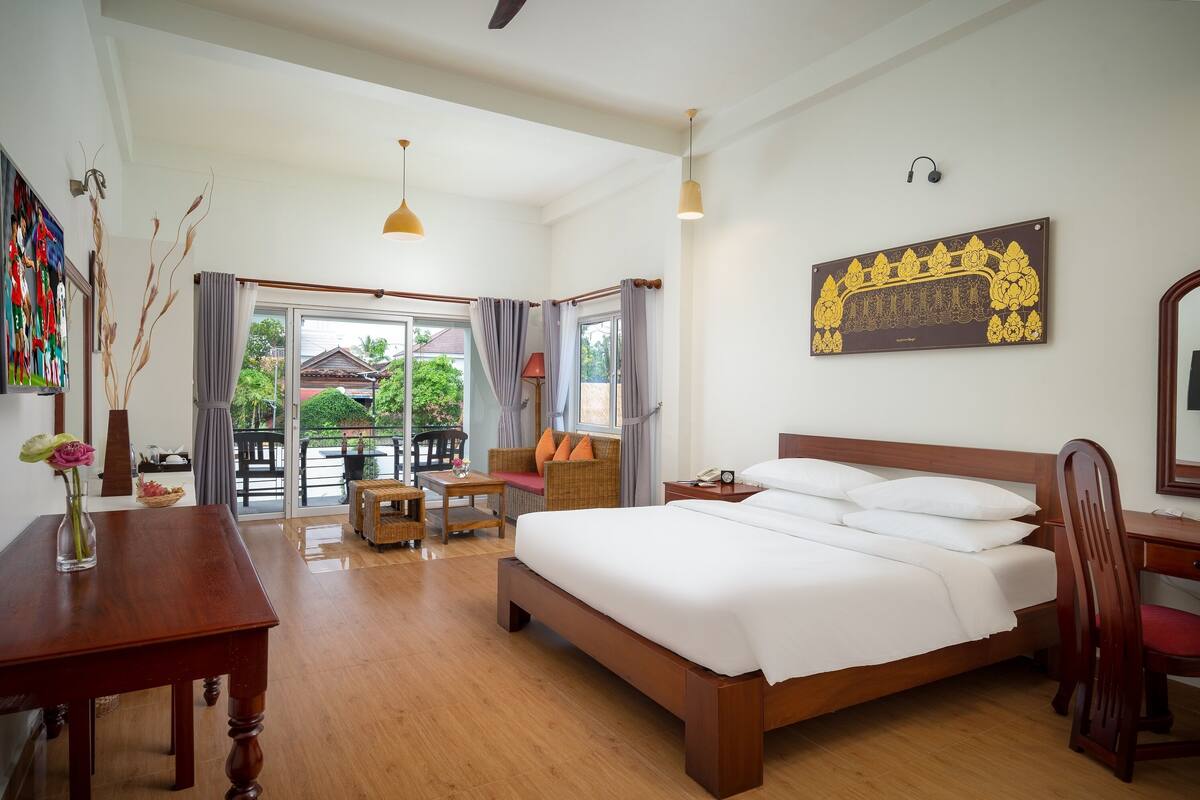 Een hotelkamer met een groot bed, houten meubels, een eettafel en uitzicht op de omgeving.