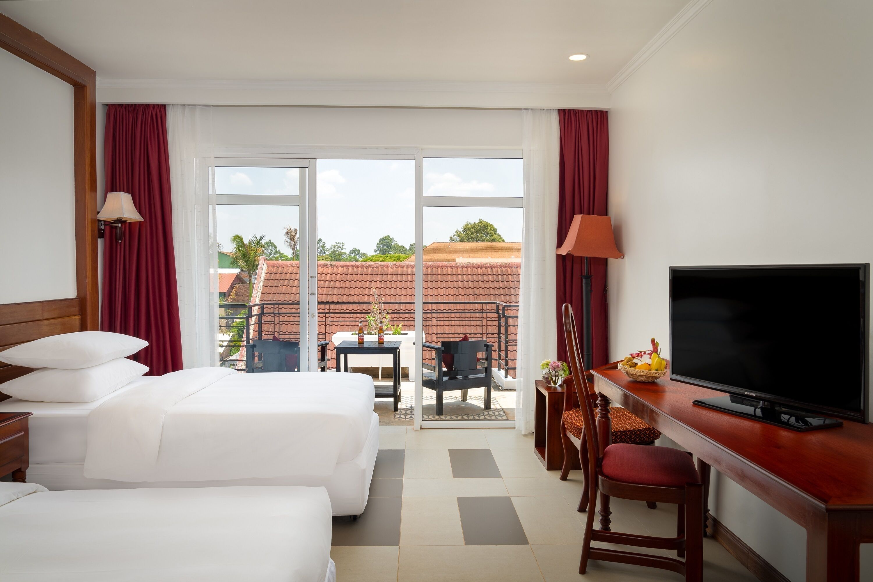 Une chambre d’hôtel avec deux lits, un bureau avec une télévision et un balcon équipé d’une table et de chaises.