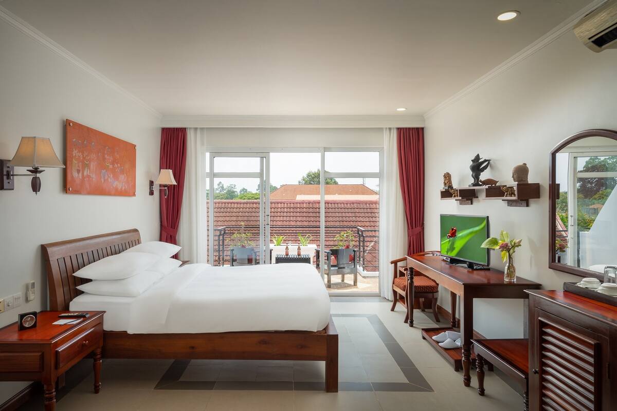 Een hotelkamer met een groot bed, een bureau met een televisie, een stoel en uitzicht op het omliggende landschap.
