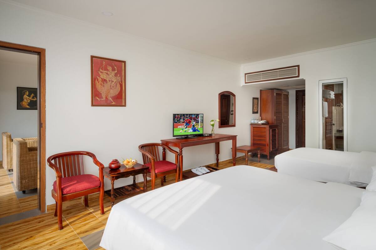 Een hotelkamer met twee bedden, een houten bureau met een televisie, een stoel en een kledingkast.