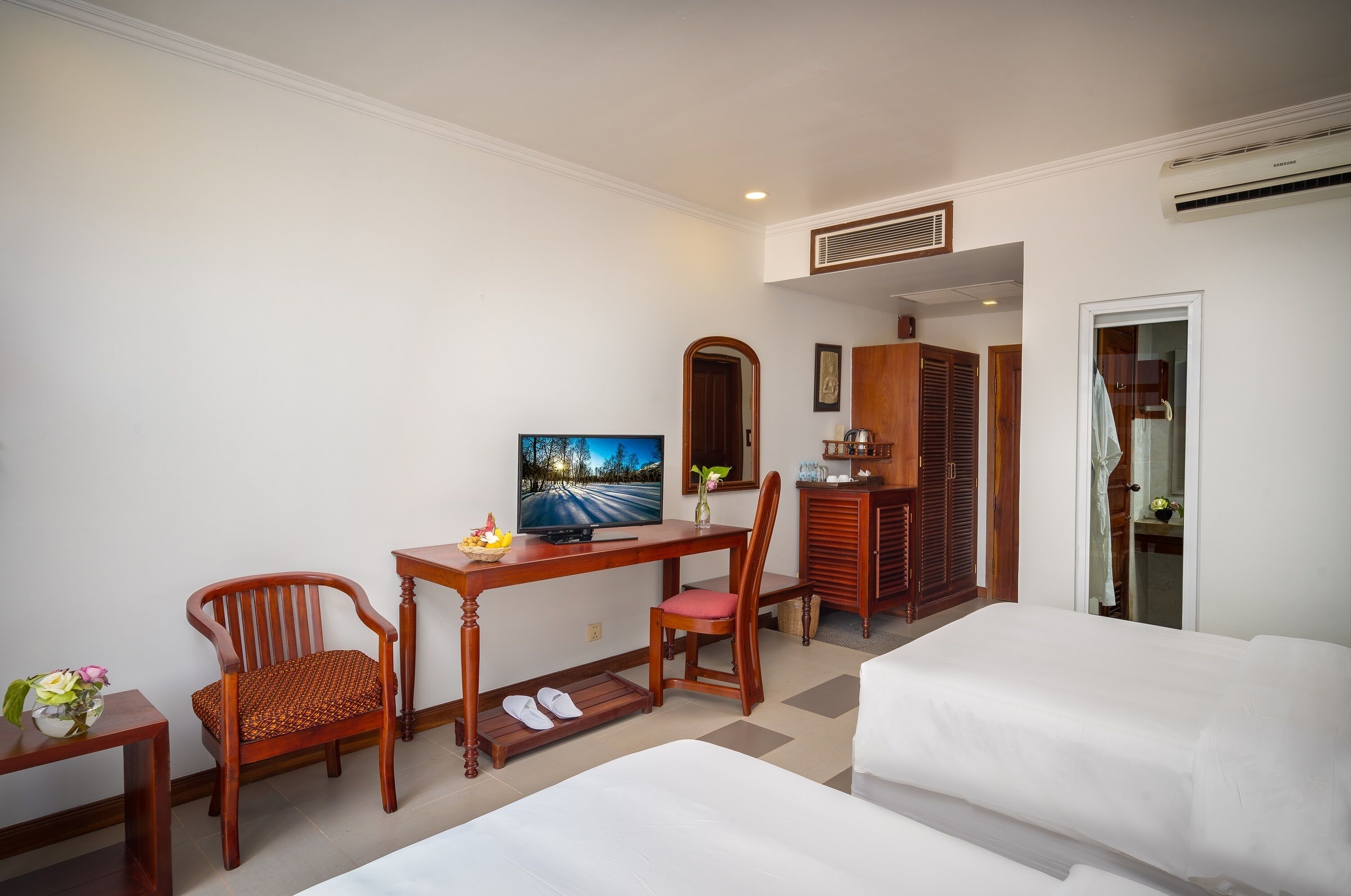 A hotel room with a bed, a desk with a TV, two chairs, a wardrobe, and a bathroom visible through an open door.