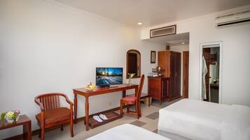 A hotel room with a bed, a desk with a TV, two chairs, a wardrobe, and a bathroom visible through an open door.