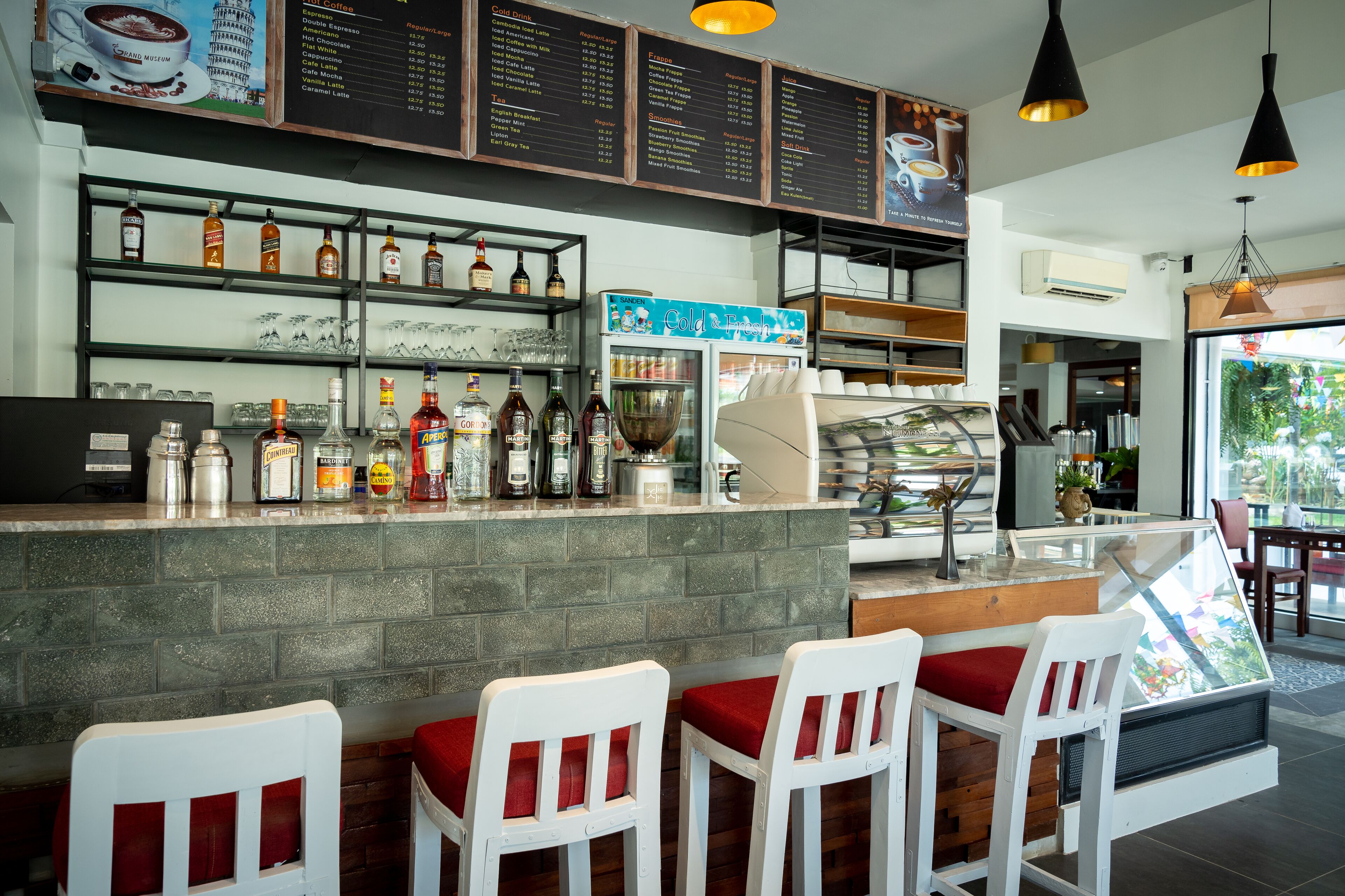 A bar area with a menu board, shelves with bottles, and white bar stools.