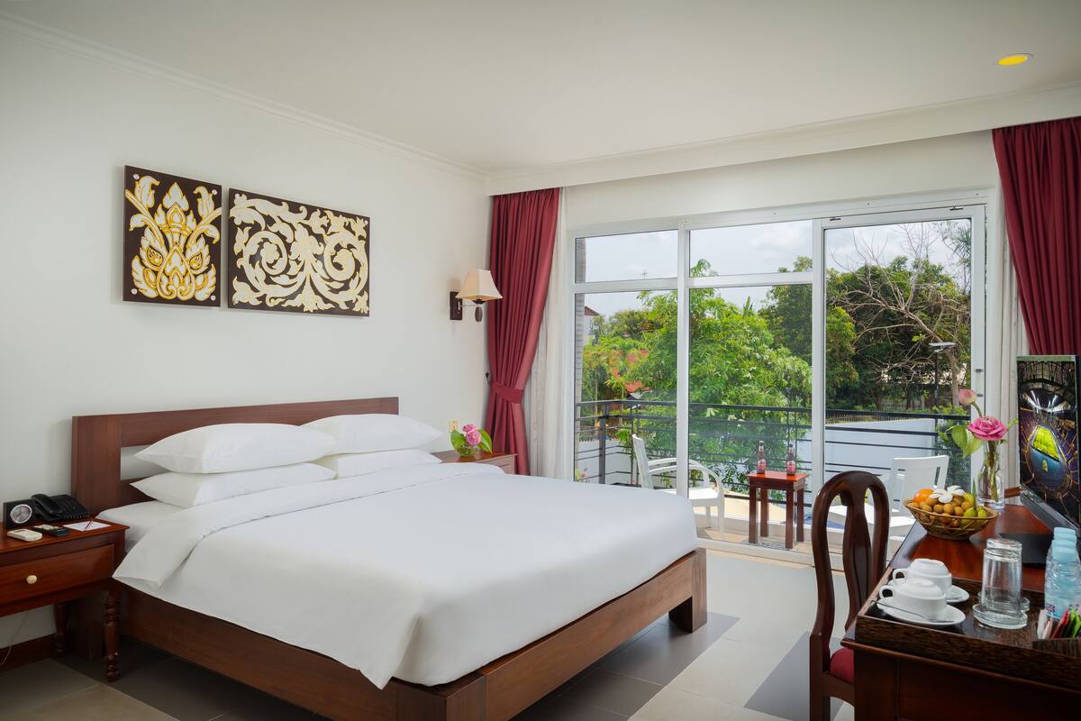 Een hotelkamer met een groot bed, een bureau met stoel, een balkon met tafel en stoelen, en kunst aan de muur.