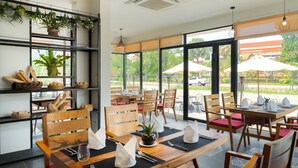 Un restaurante con mesas y sillas de madera, plantas en macetas y vistas al exterior.
