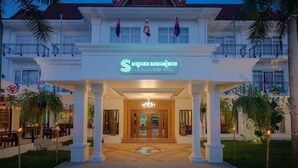 Una entrada de hotel de estilo arquitectónico tradicional, con un acceso destacado, banderas y una fachada bien iluminada.