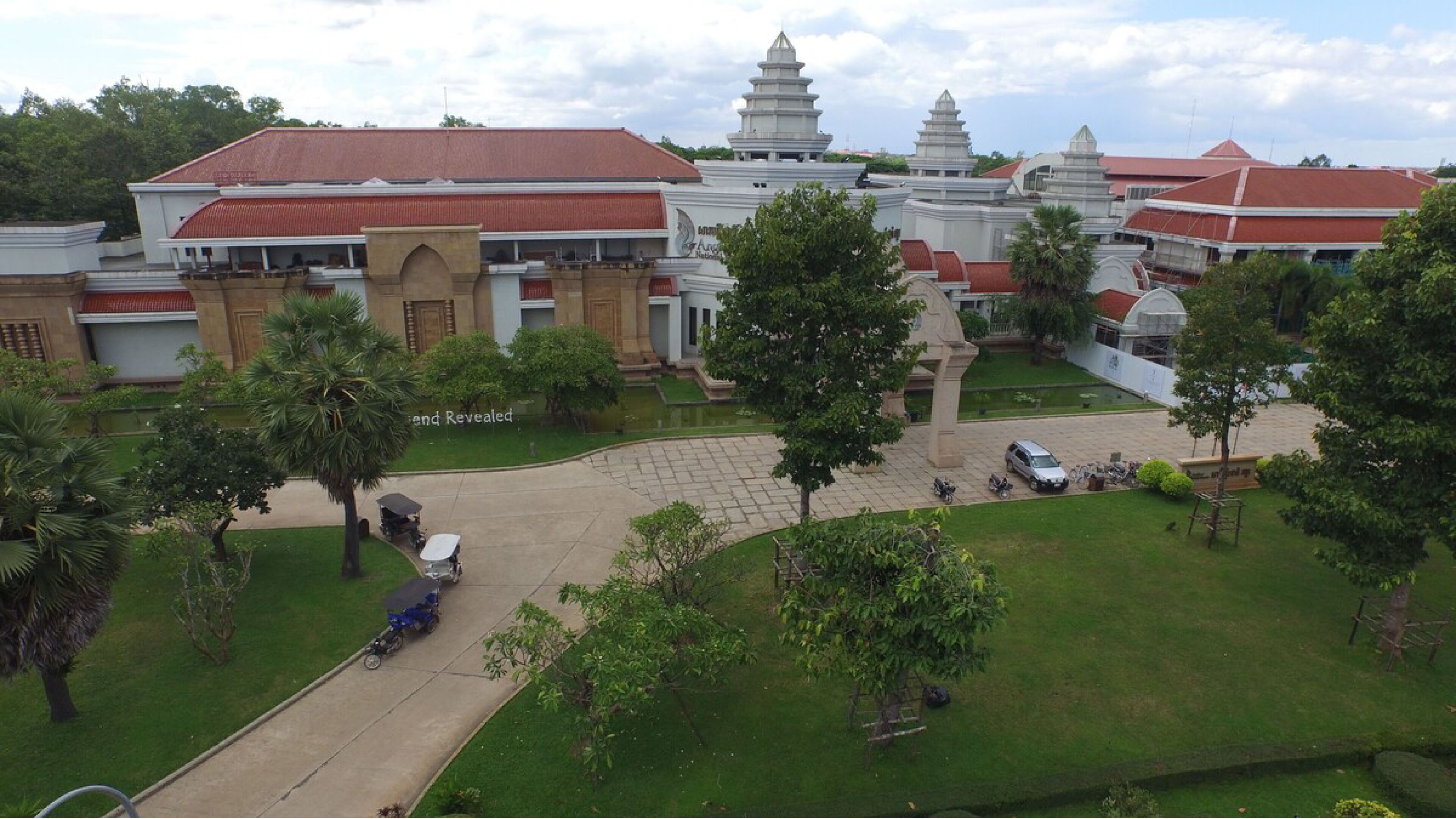 A large, traditional building with multiple pagoda-style structures, surrounded by well-maintained lawns and trees.