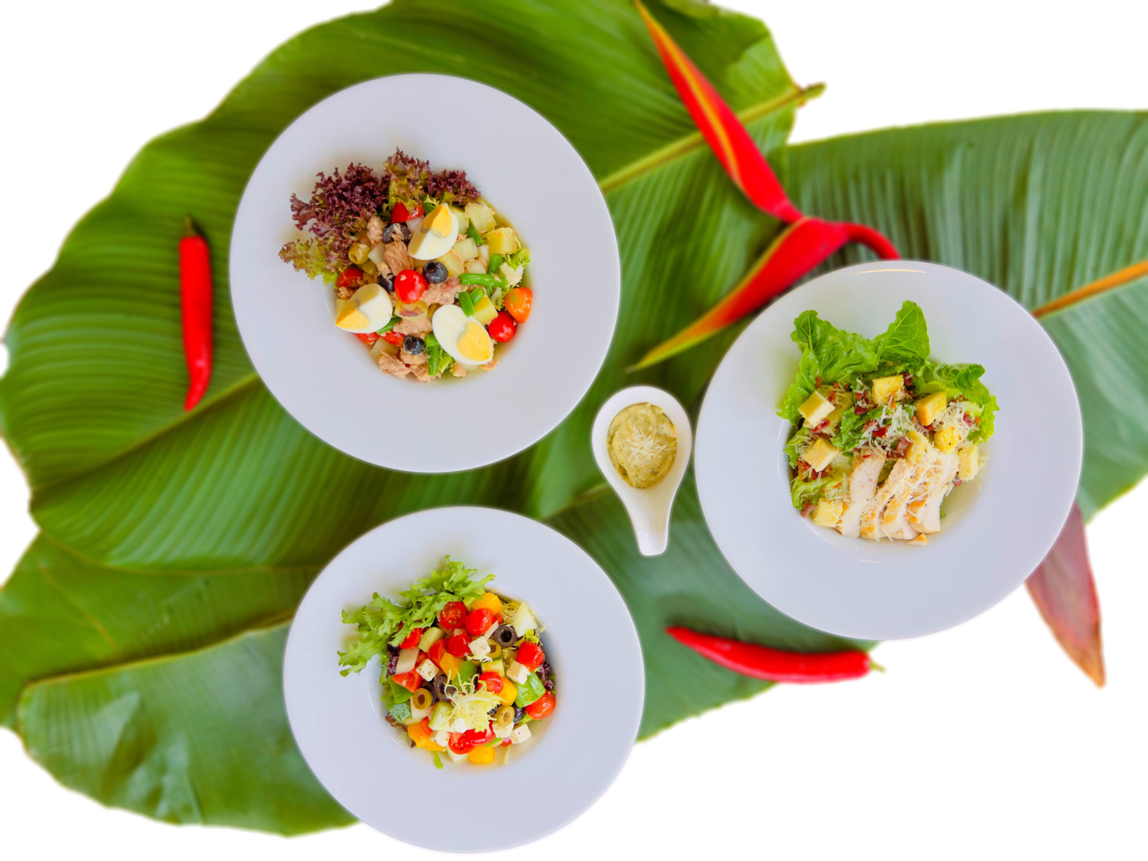 Tres platos blancos de ensalada con diversos ingredientes, sobre una hoja verde grande.