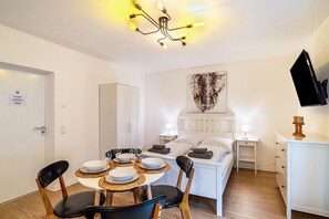 A bedroom with a bed, bedside tables, a TV, and a dining area with chairs and a table.